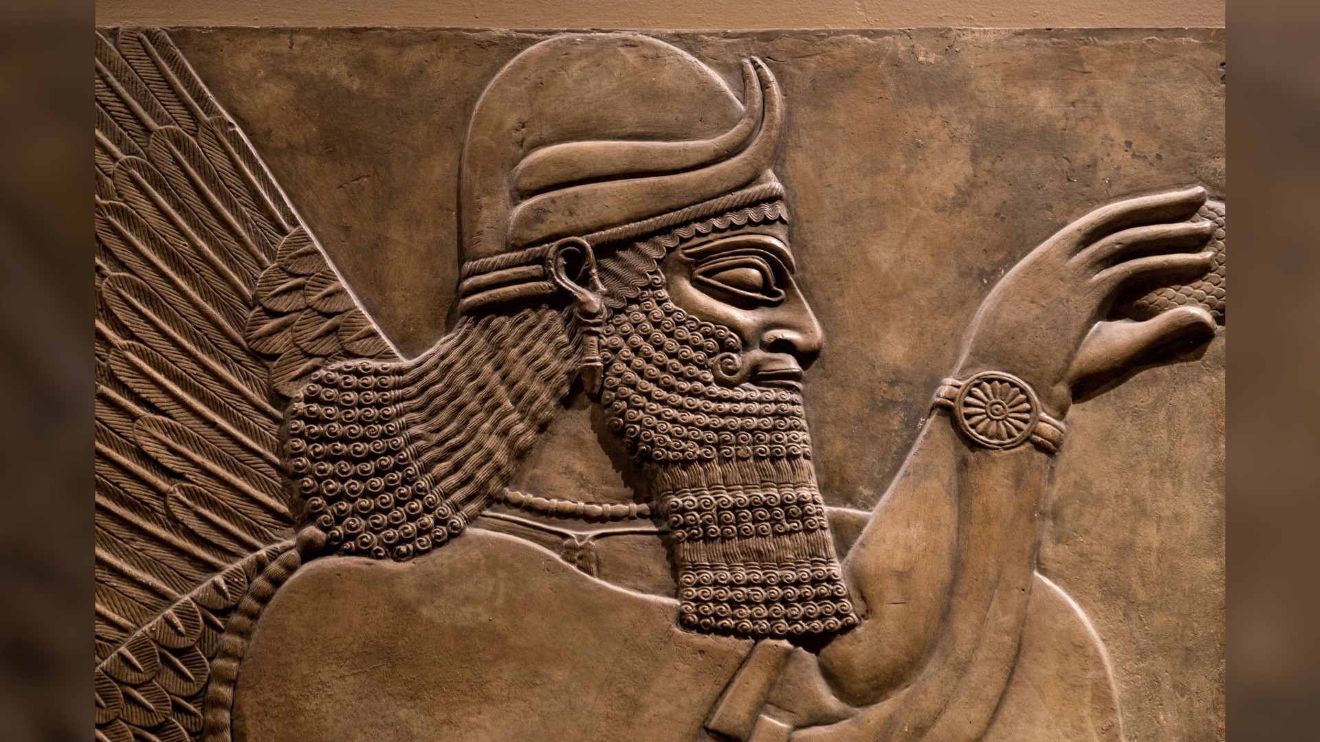 Ancient relief of an Assyrian god. Here we see a side profile of a man with long hair, a long beard and wearing a helmet.