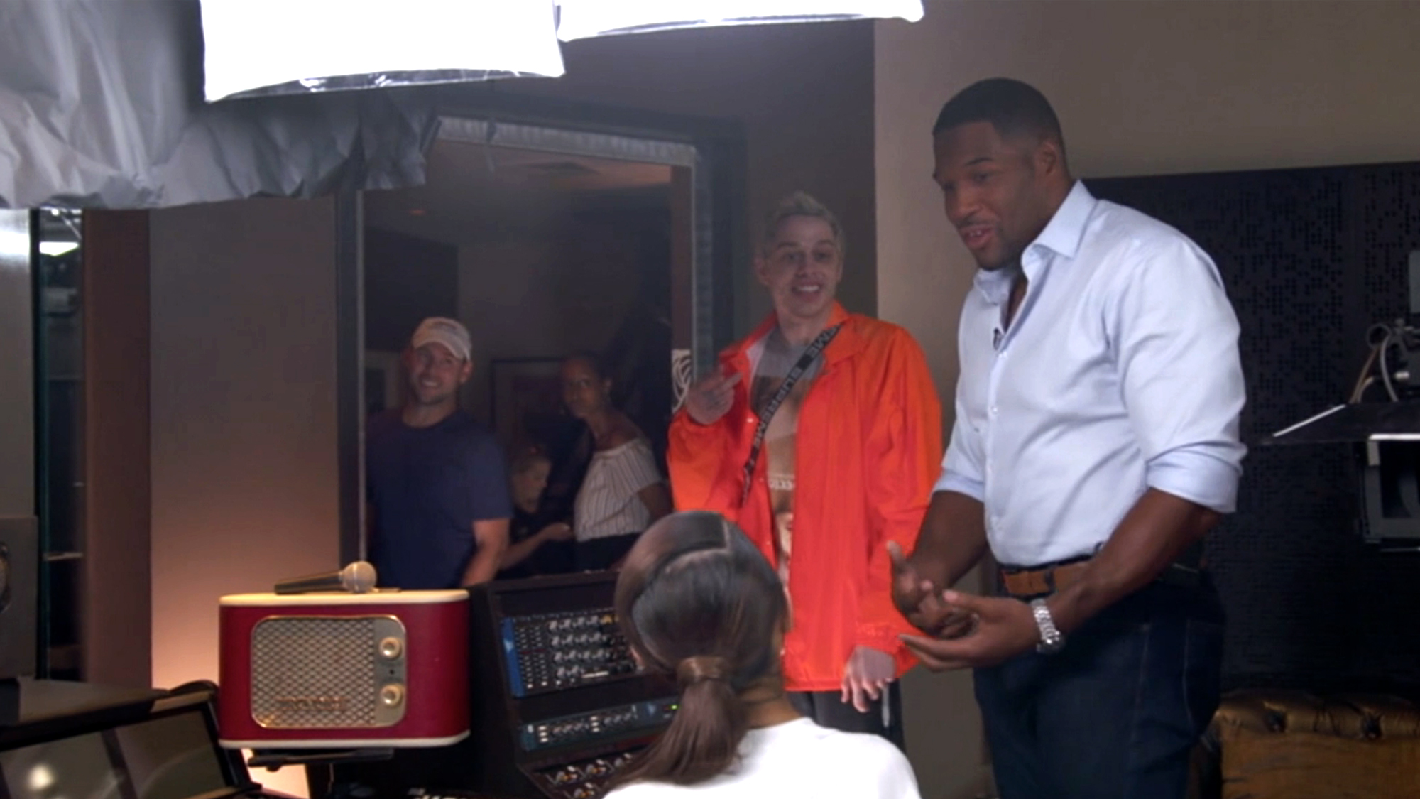 In a behind-the-scenes moment shared in 9/11: United We Stand, Davidson in an orange Jacket, Strahan in a blue open button-up, and the back of Grande, the group shares an unforgettable moment.