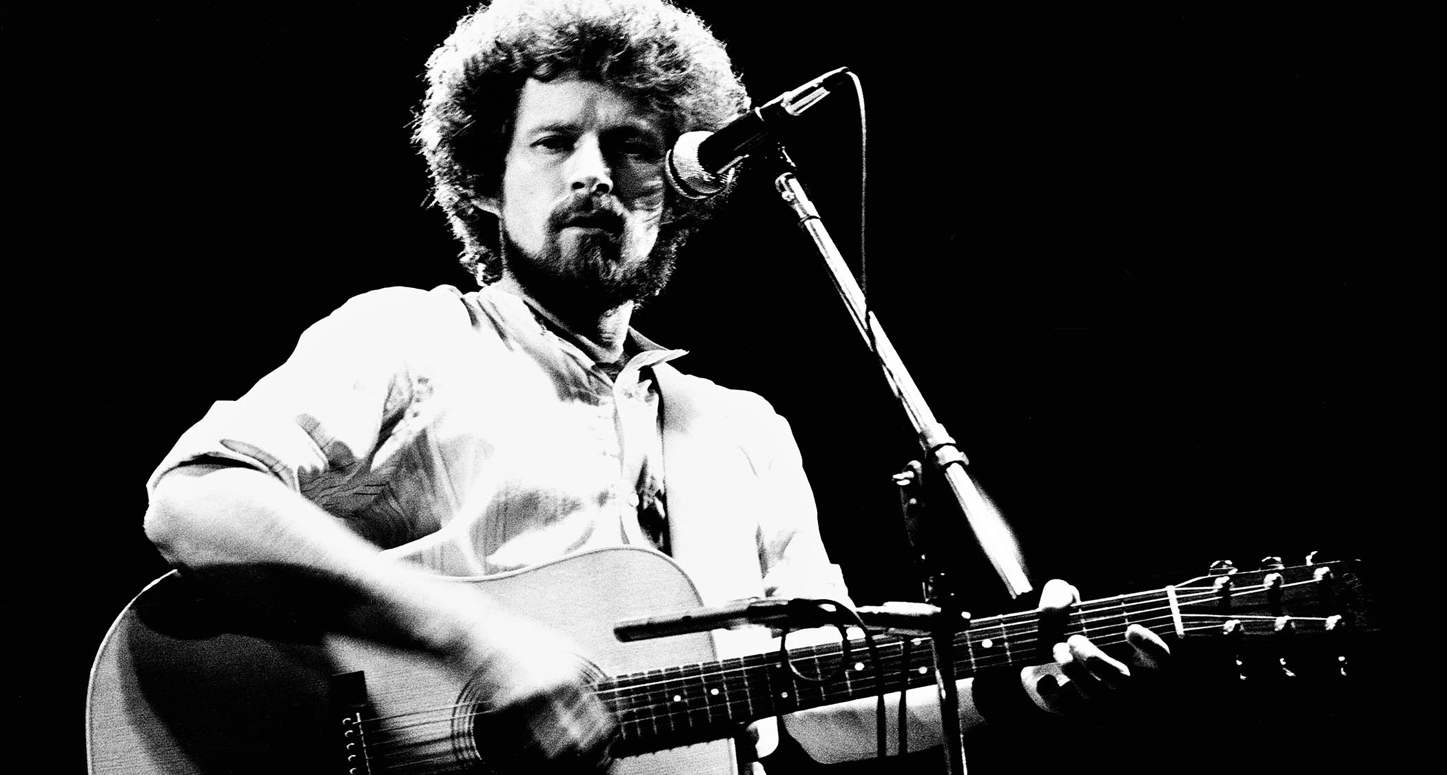 Don Henley plays an acoustic onstage with the Eagles in 1977