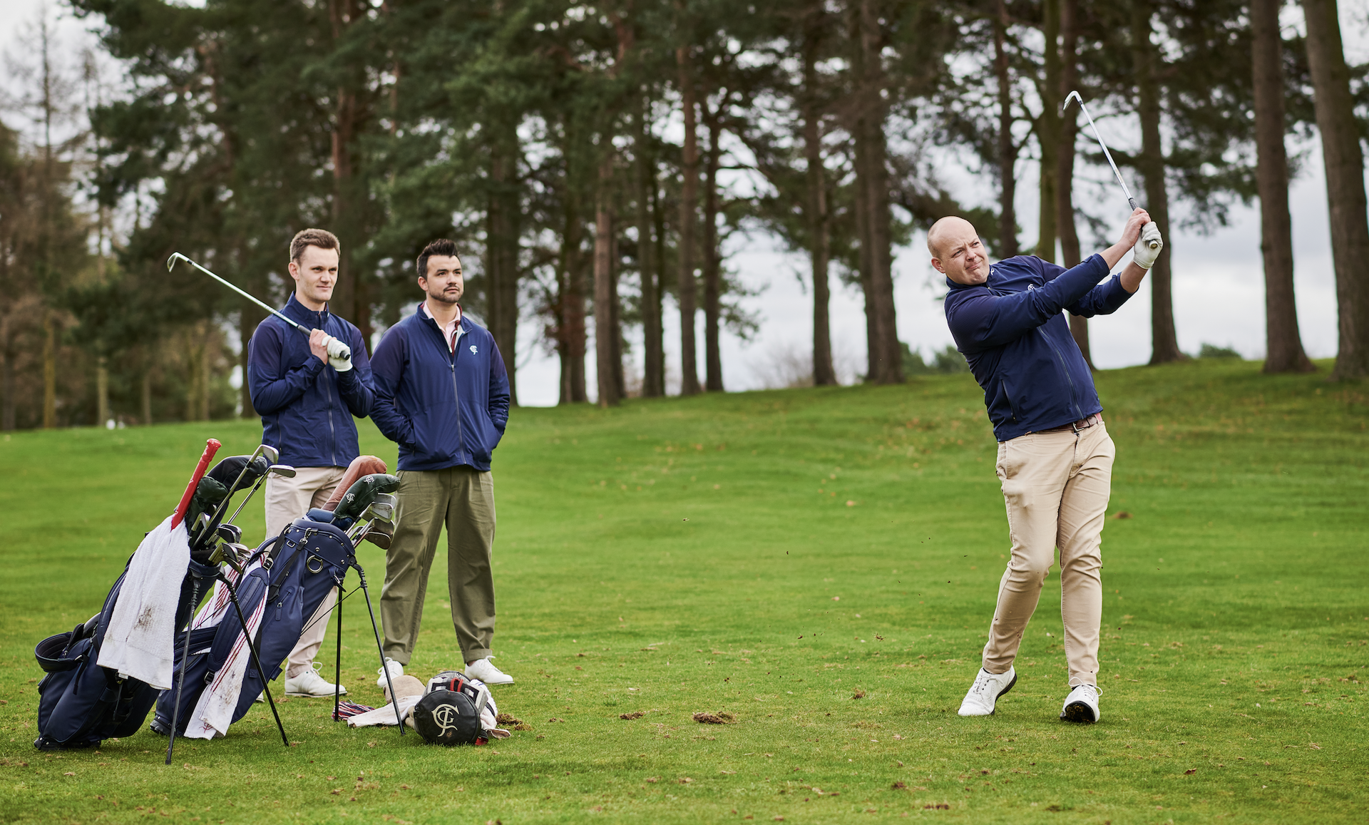 Golfer hits a shot with two playing partners watching on