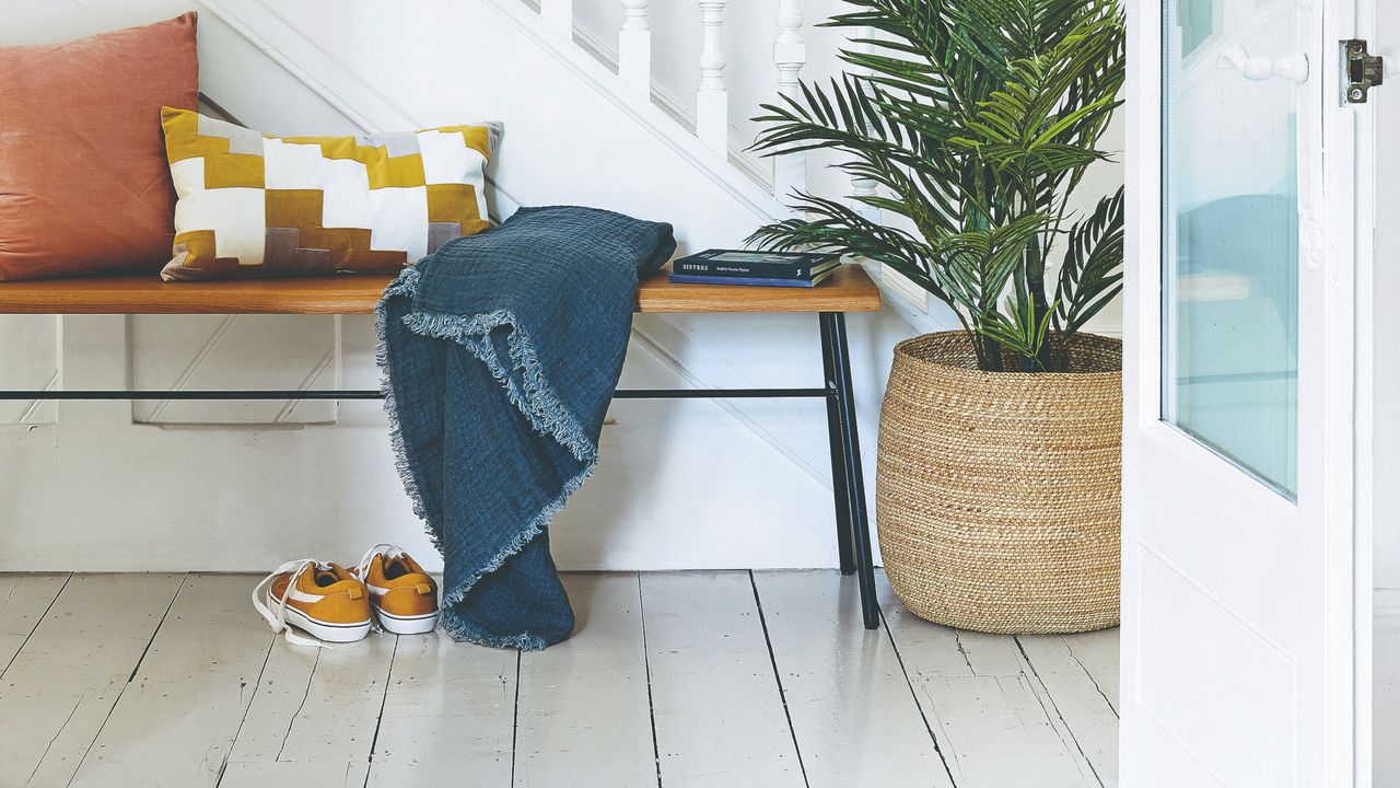 A hallway with a simple shoe bench and a wooden floor boards painted white