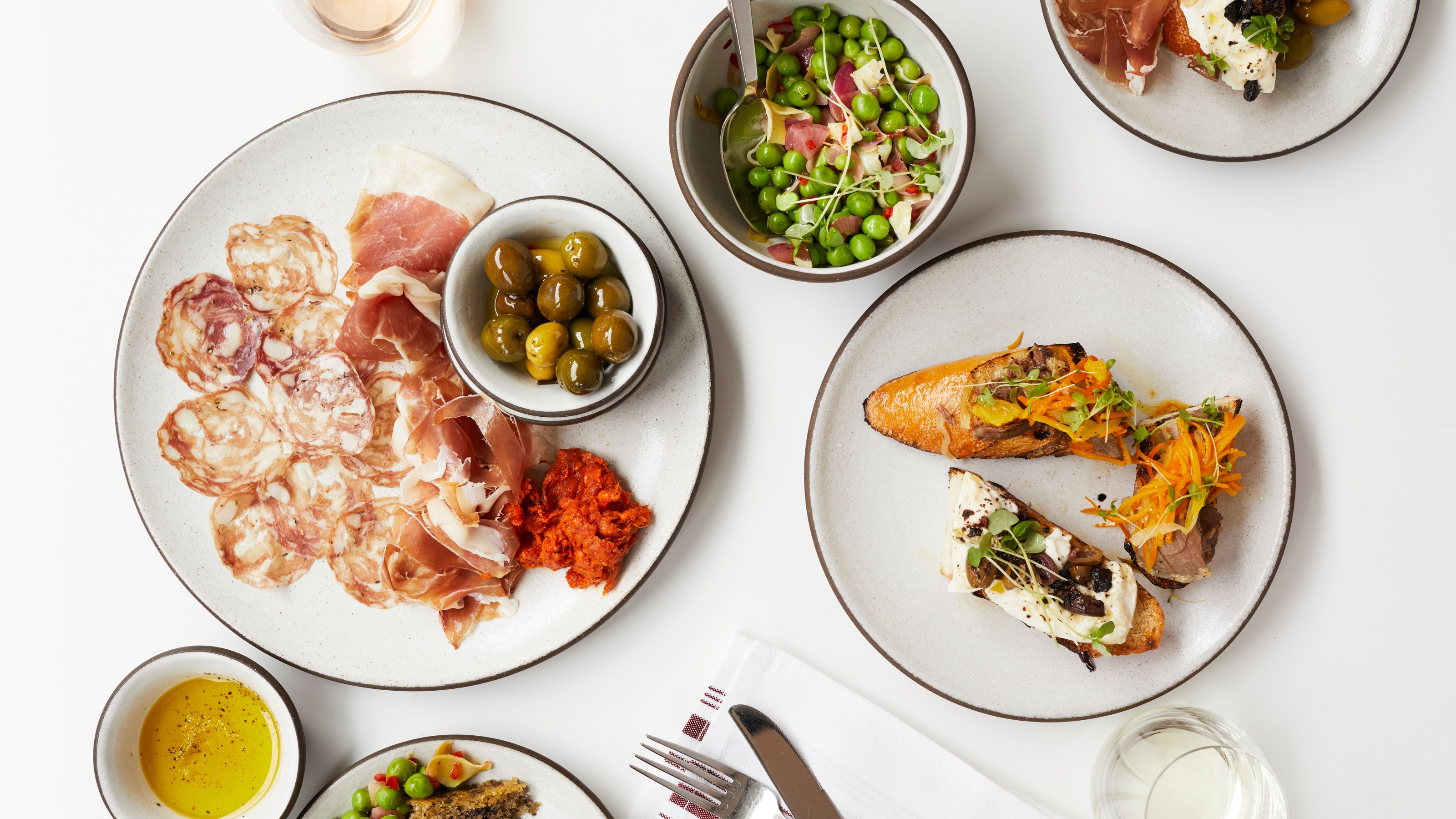 Image of a white background and a mix of white dinner plates and bowls with a dark trim. The pieces are all filled with different gourmet food items. 