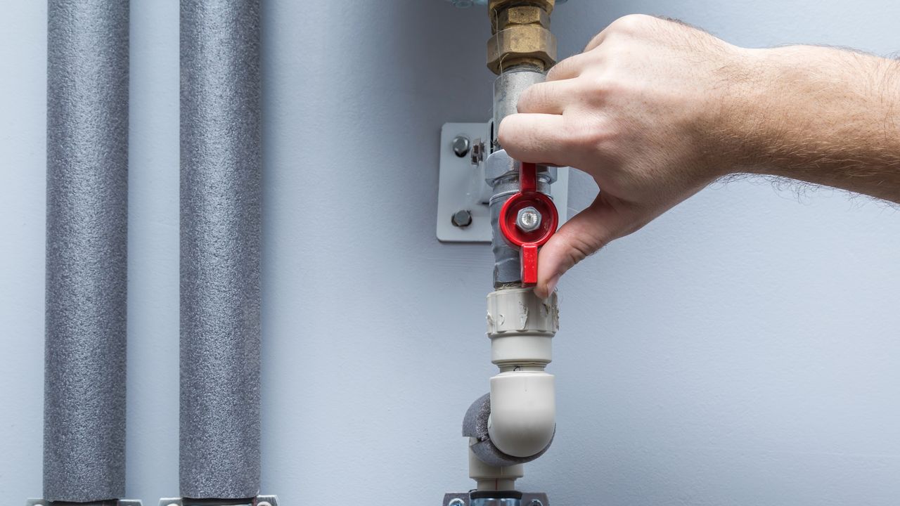 Hand turning red stopcock vertically on grey water pipe