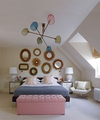 An example of bedroom ceiling light ideas showing a black bed in front of decorative gold wall mirrors and below a large blue, pink and green ceiling light