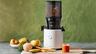 A Hurom H320 juicer next to a glass of juice and and ingredients