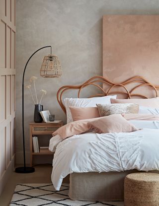 Blush bedroom with white bedding, and organic, curvy headboard, with standing floor lamp and woven shade.