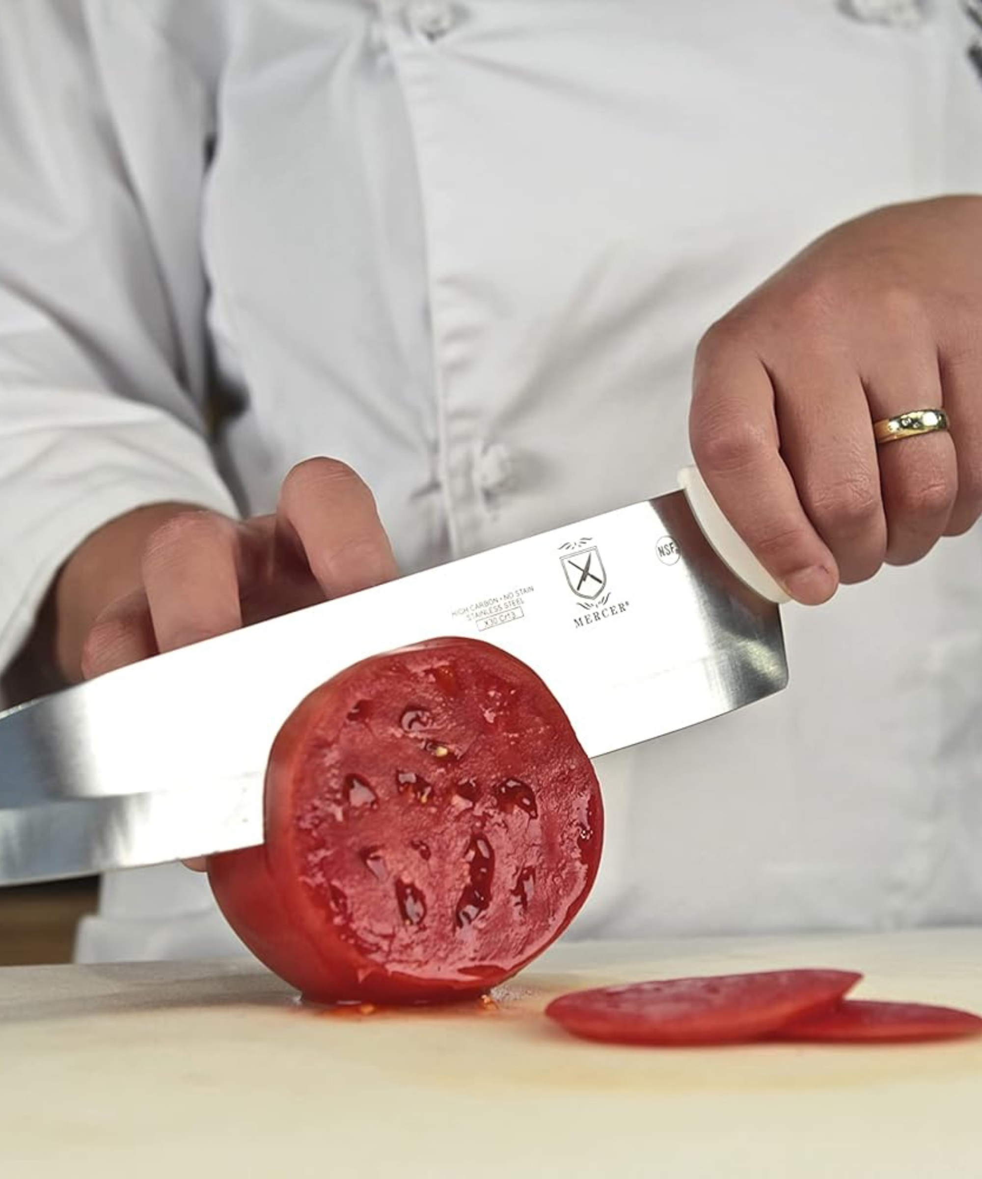 A white Mercer chef's knife slicing a tomato