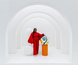 Nicole Moyo in red, beside giant colourful sculpture in white space