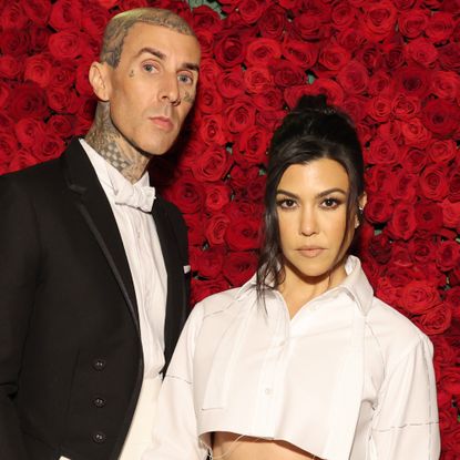 Travis Barker and Kourtney Kardashian in front of a red roses background at The Met Gala
