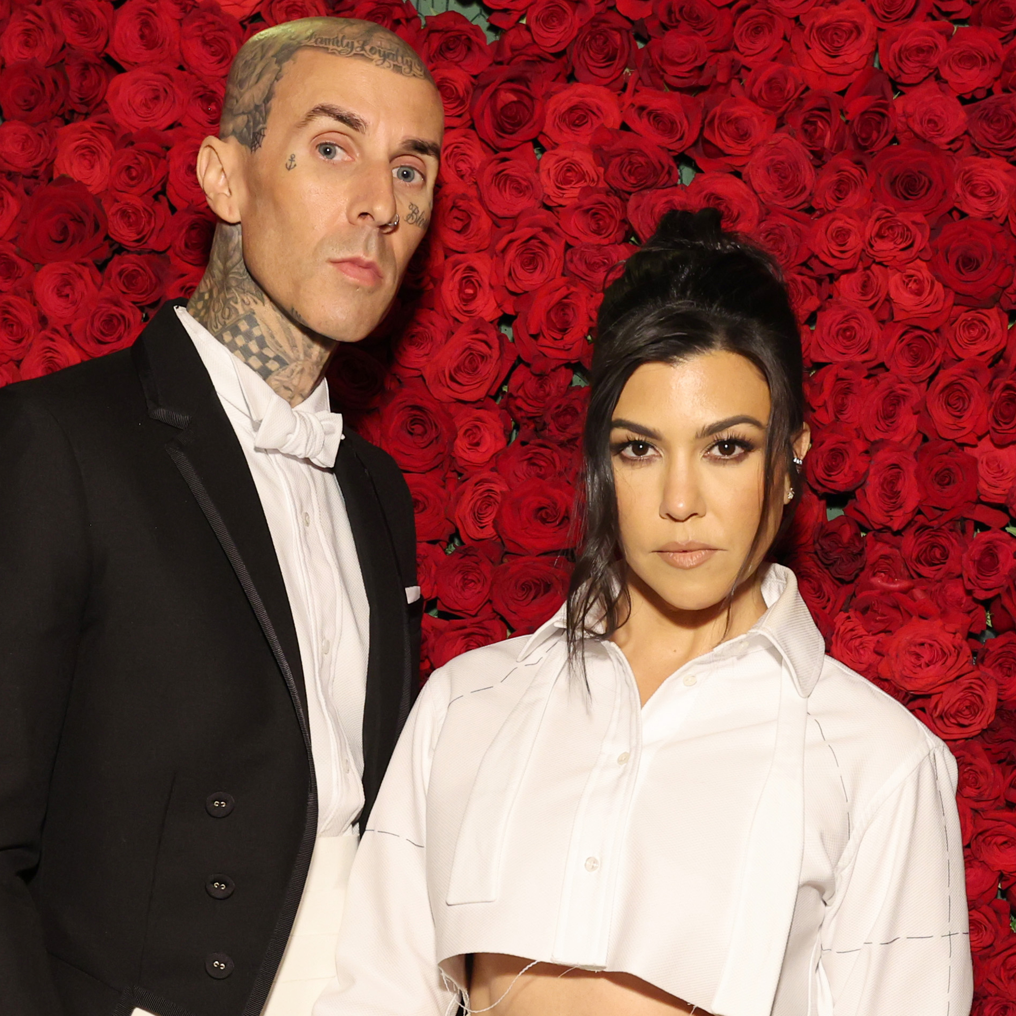 Travis Barker and Kourtney Kardashian in front of a red roses background at The Met Gala