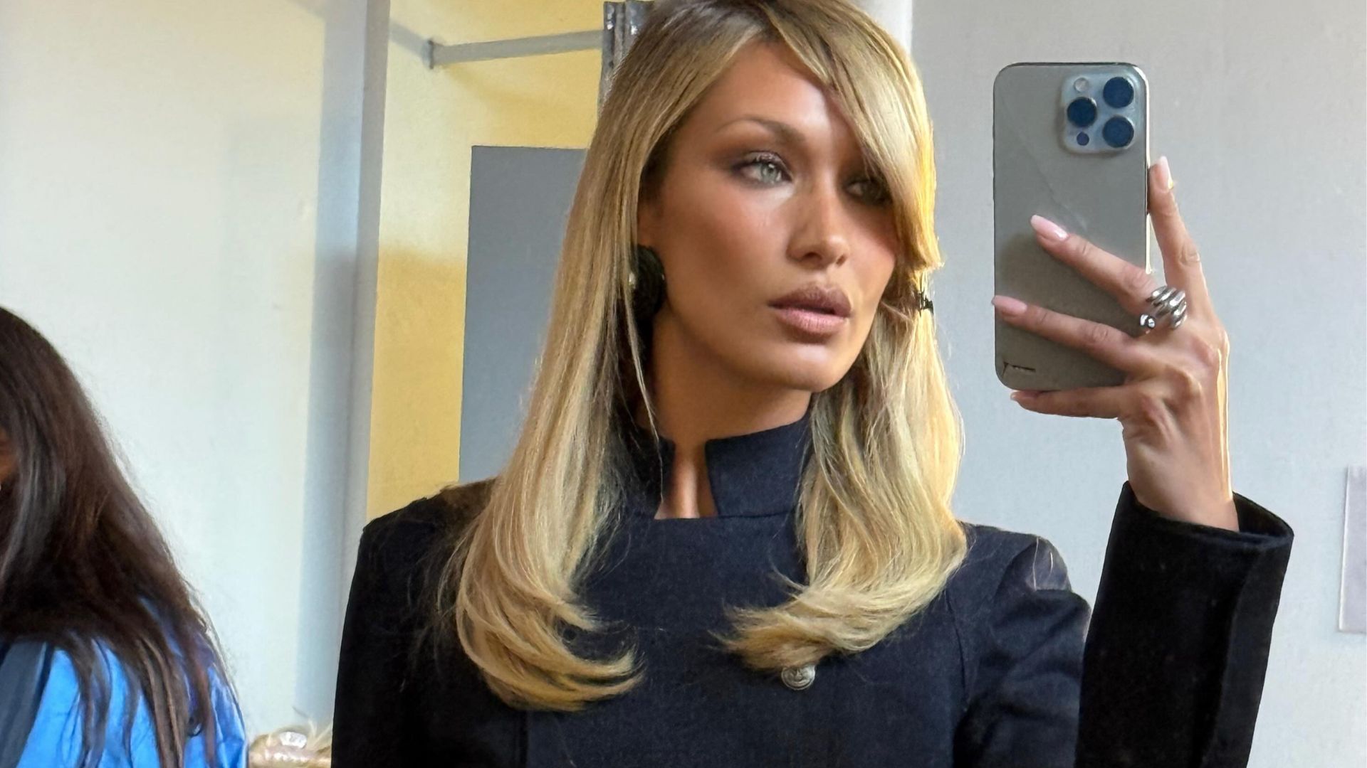 Bella Hadid takes a mirror selfie wearing a cropped military jacket with a low-rise denim skirt.