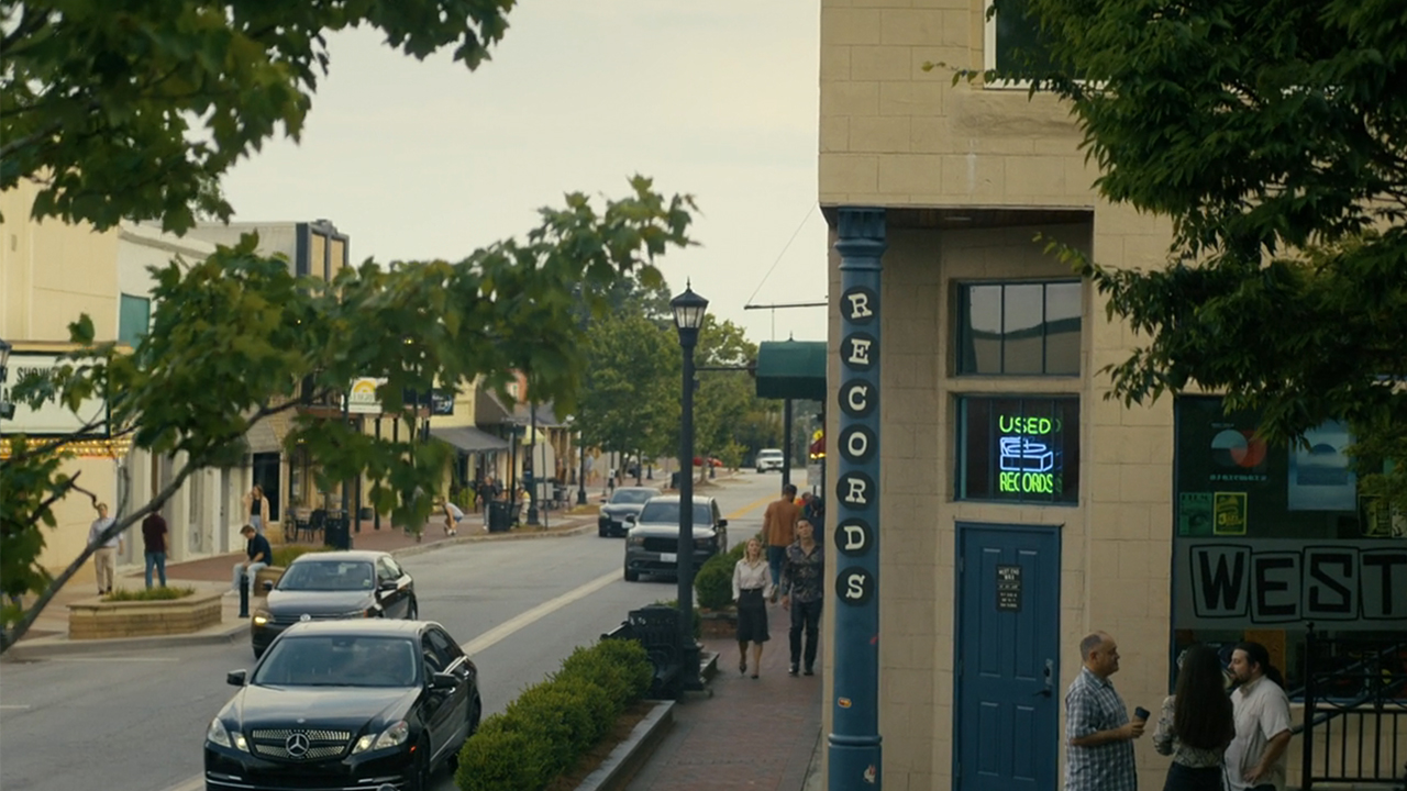 A street scene in Peacemaker with two characters walking past a record store