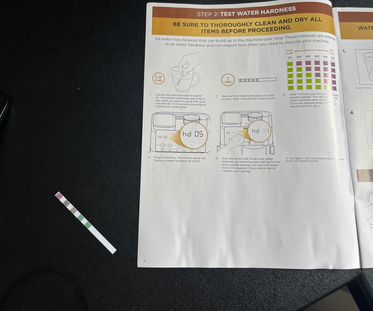 A close up of a water hardness test strip on a black kitchen counter beside the manual.