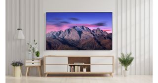 An LG B5 TV showing an image of a mountain range at dusk. The TV is wall mounted in a bright room above a TV unit