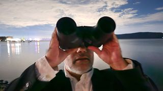 A man looking up at the night sky with the Unistellar Envision smart binoculars with water in the background.