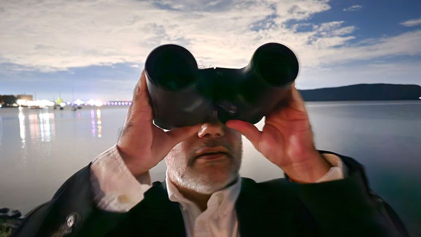 A man looking up at the night sky with the Unistellar Envision smart binoculars with water in the background.