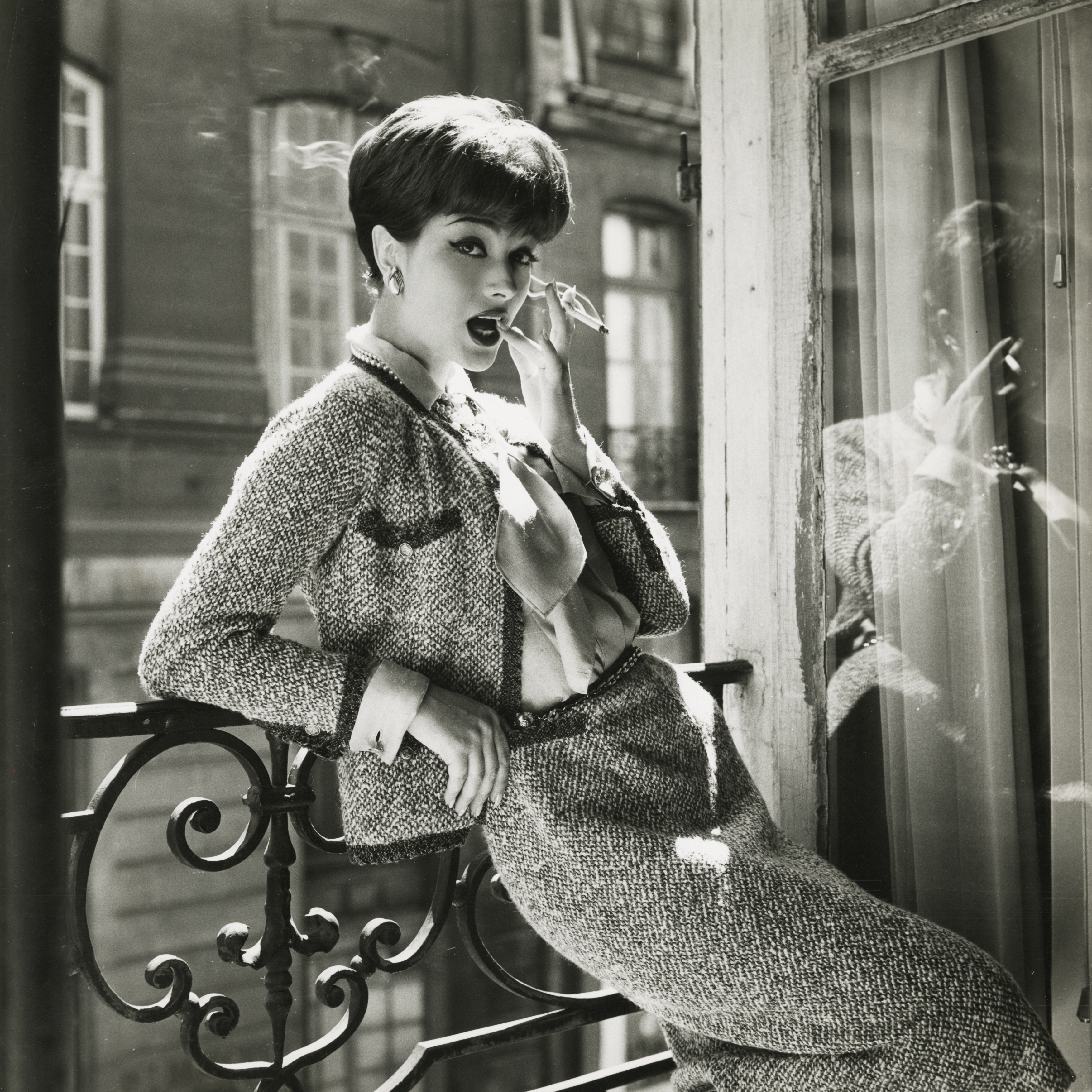 Model Marie-H&amp;eacute;l&amp;egrave;ne Arnaud leaning on balcony in Coco Chanel's apartment above her Paris salon in 1958, wearing a tweed Chanel suit