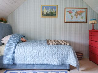 boy's bedroom with blue patterned quilt, artwork, red chest of drawers, loft ceiling