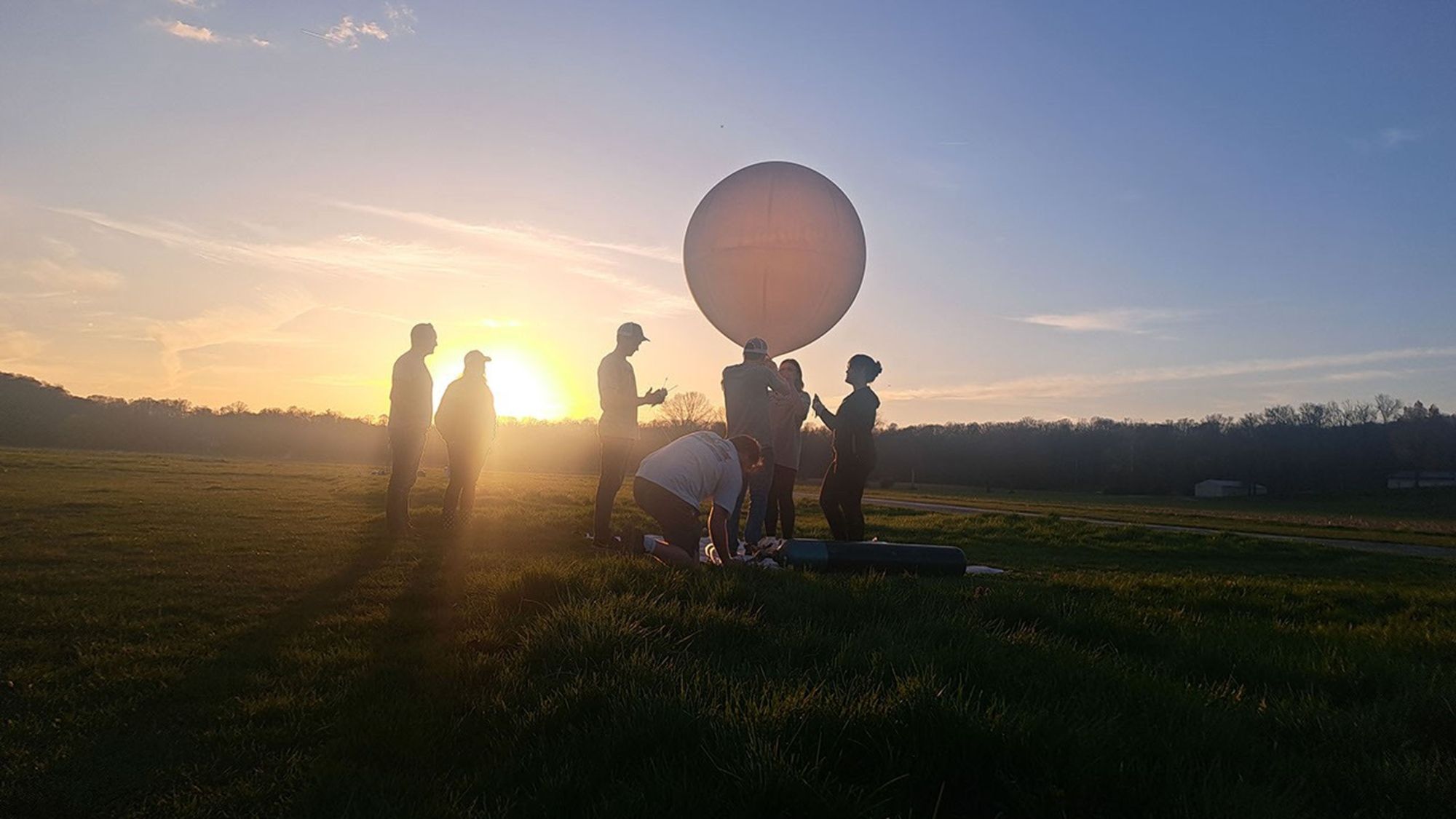 People are seen as silhouettes with the sun behind them. They're on a field.
