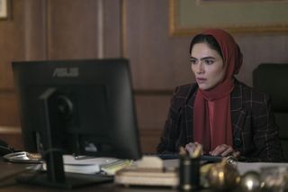 Arienne Mandi as noor sitting at a desk and computer in a still from the night agent