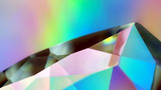 A close-up image of a diamond's shimmering facets on a rainbow background
