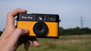 Photograph of man's hand holding Camp Snap 2 digital camera, in yellow colorway