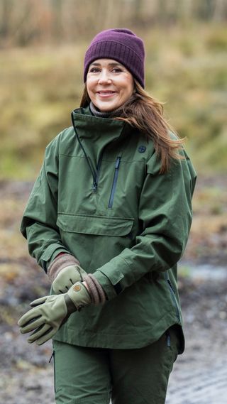 Queen Mary wearing khaki waterproof co-ord, plum beanie and green gloves