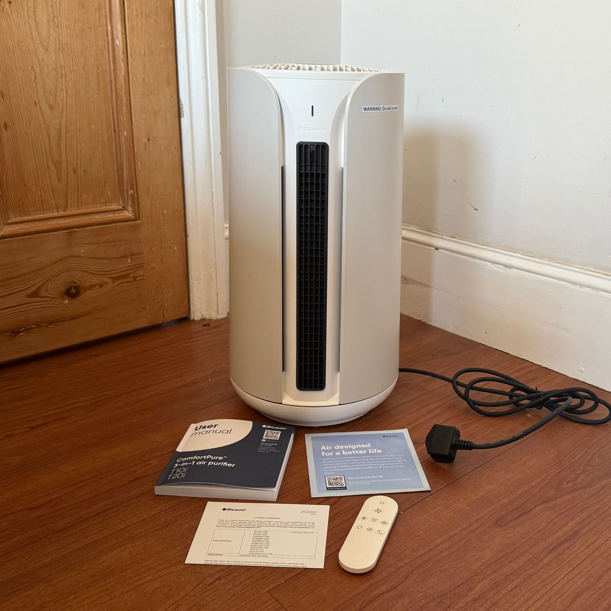 Blueair ComfortPure 3-in-1 T10i Air Purifier on wooden flooring with instruction manual and control in front of it