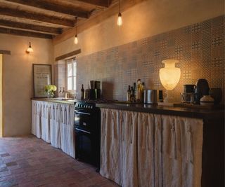 A French country kitchen with cabinet curtains and layered lighting