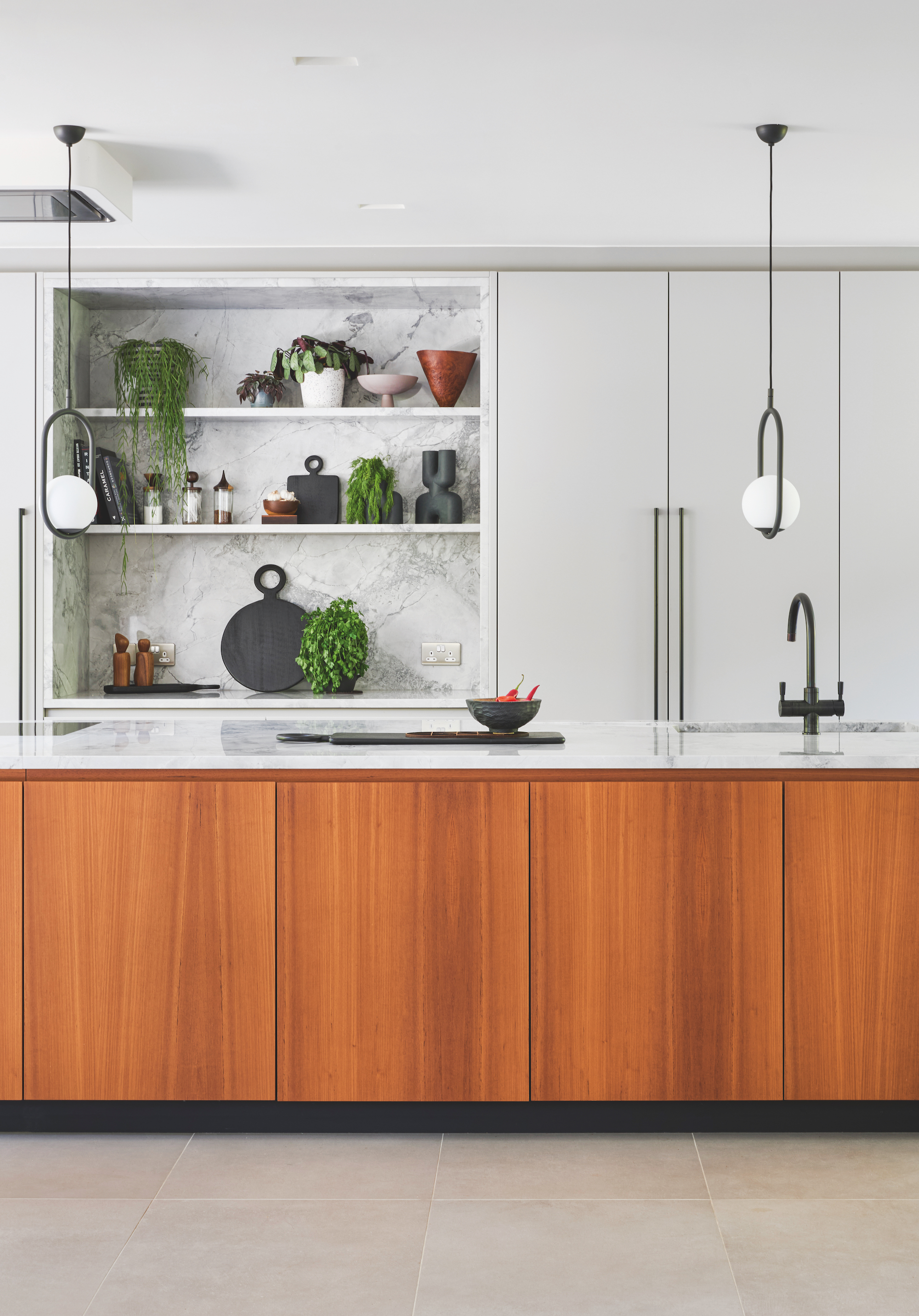 A modern style kitchen with a warm tone wooden kitchen island with a white marble work top, and two pendant lights above.