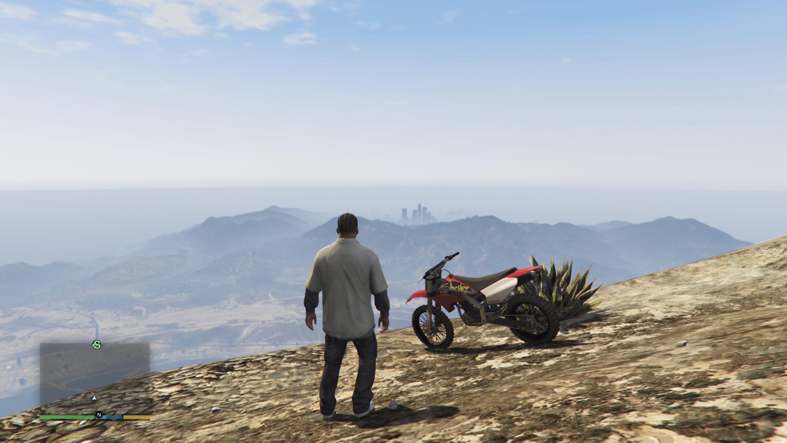 A screenshot of GTA V picturing Franklin and a dirt bike on a mountain