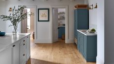 A blue and white kitchen with white walls and light engineered hardwood flooring.