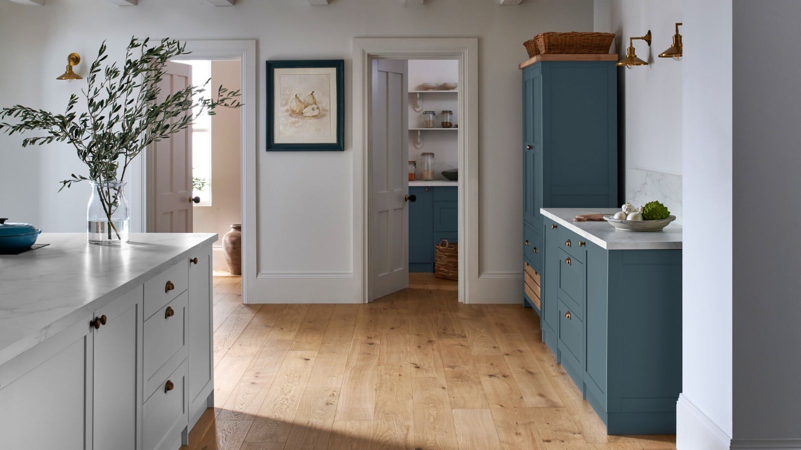 A blue and white kitchen with white walls and light engineered hardwood flooring. 