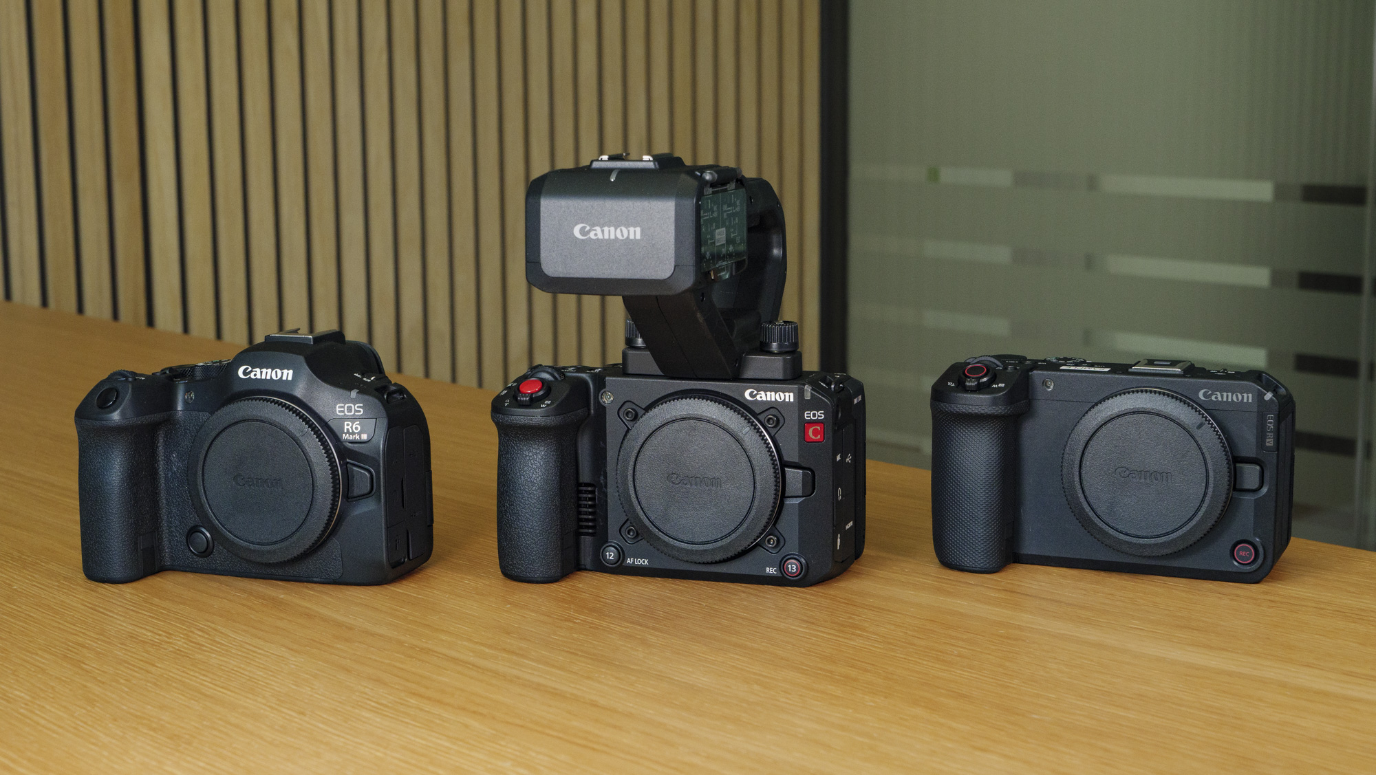 The Canon EOS R6 V on a wooden table alongside the Canon EOS R6 III and EOS C50