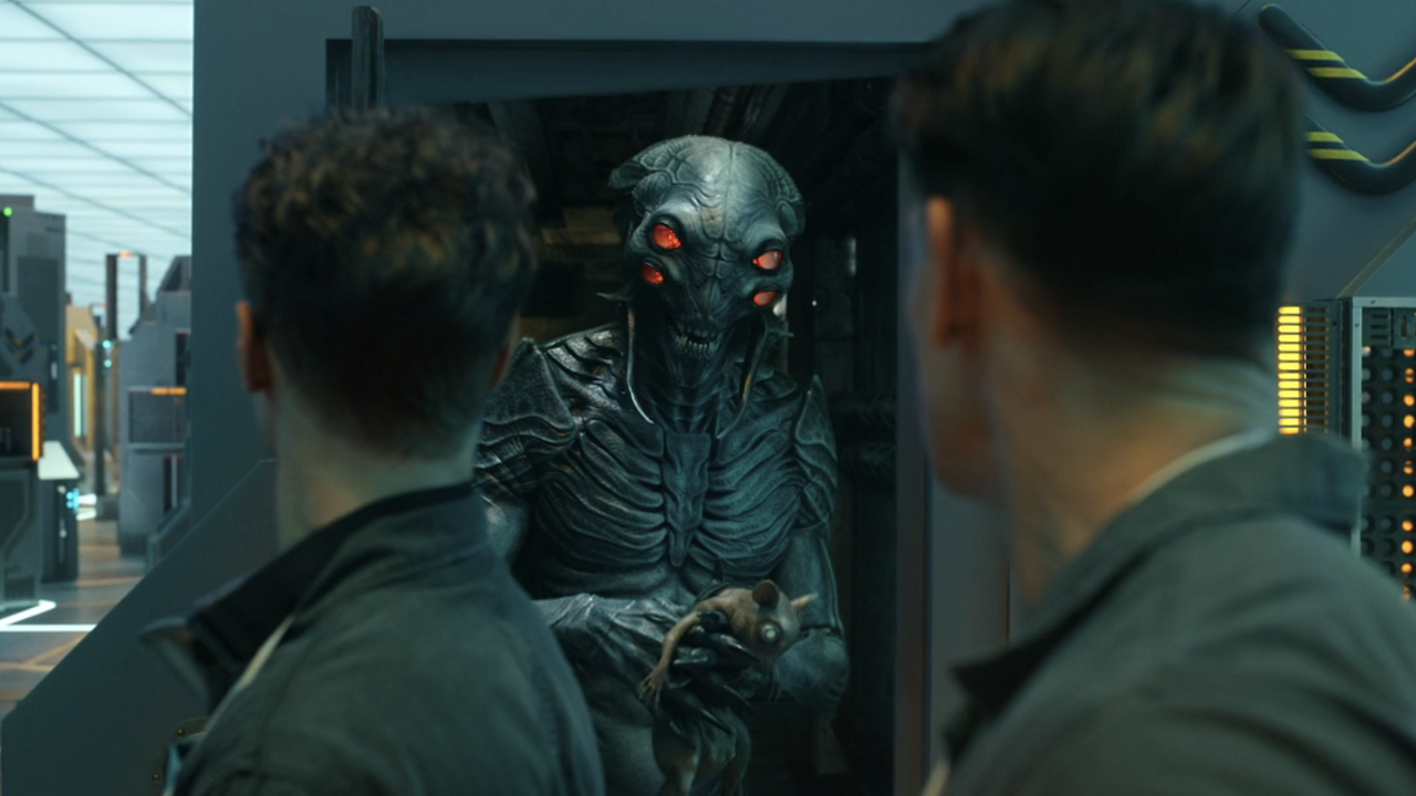 Alien holding small pet while Chris and Vigilante stare at it in Peacemaker Season 2