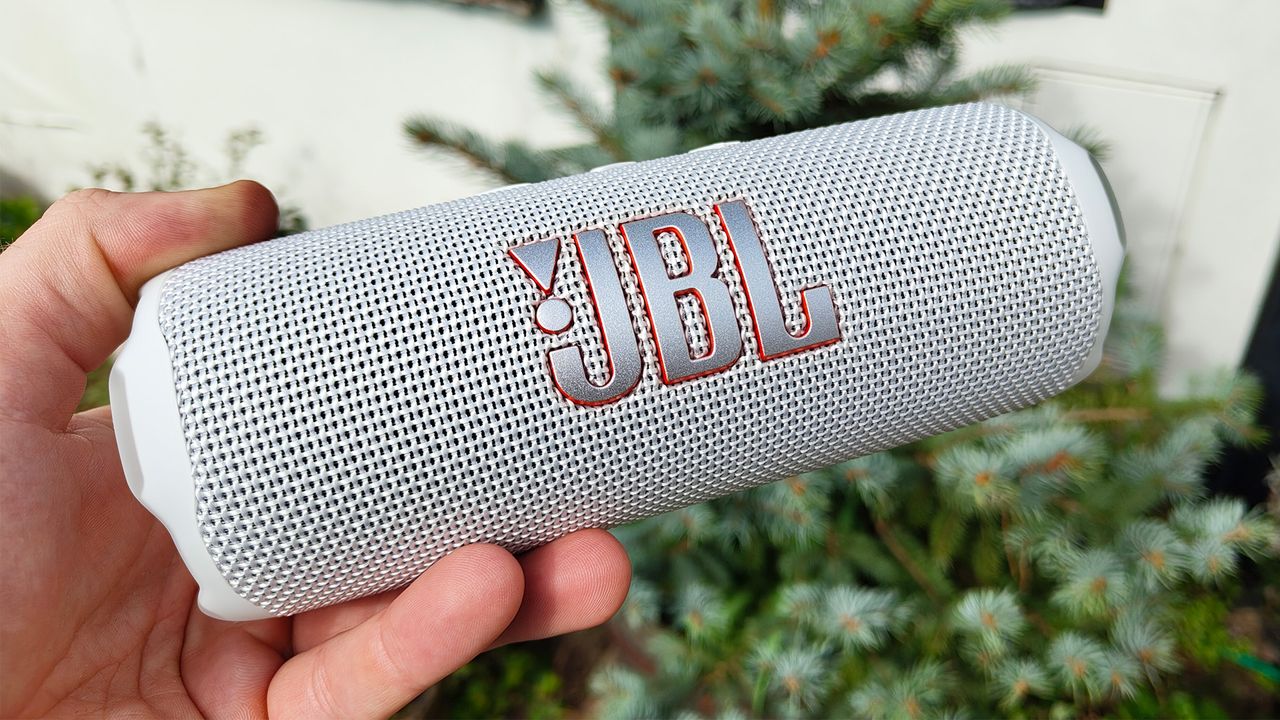 A white JBL Flip 7 wireless speaker being held by one end.