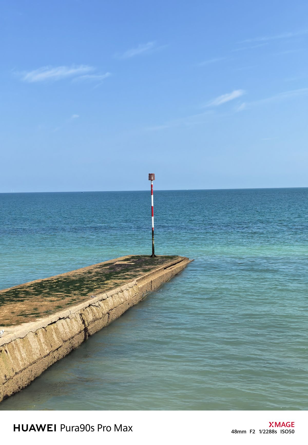 Medium view of a concrete groyne leading toward a striped navigation marker in the sea.