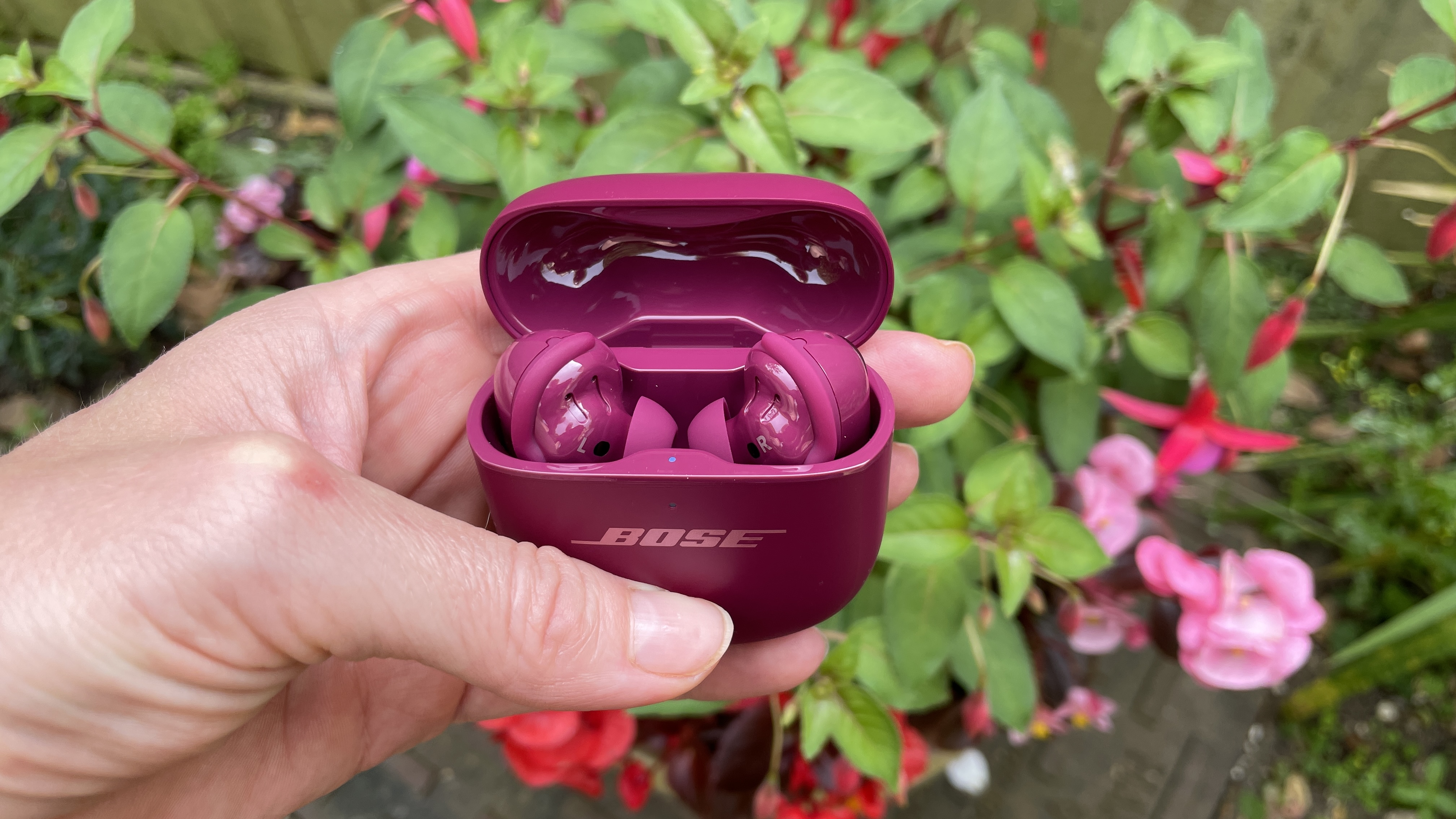 Bose QuietComfort Ultra Earbuds (2nd Gen) in purple color, next to some flowers of a similar shade but held in a hand