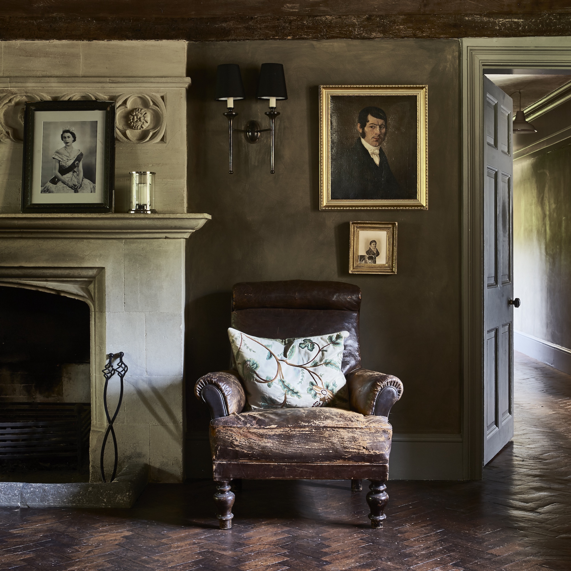 hallway in country manor house with stone fireplace, vintage leather chair, parquet wooden flooring and oil painting on wall