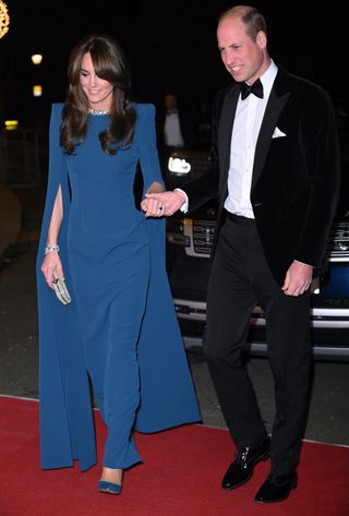 Kate Middleton wearing a blue evening gown walking the red carpet next to Prince William in a tuxedo