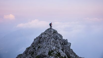 A man stands on a very high mountaintop at twilight.