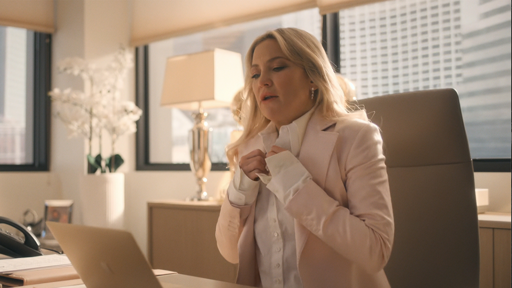 Kate Hudson sitting at a desk, looking at a computer in Running Point
