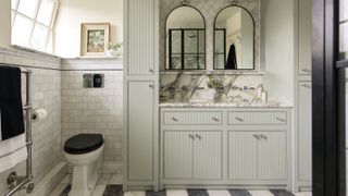 bathroom with pale green built in storage, black and white tiled floor, white wall tiles and chrome towel rail