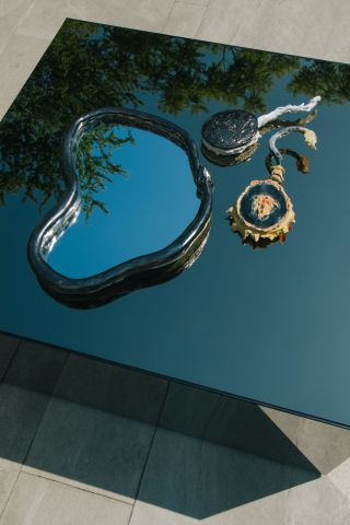 Three ceramic mirrors photographed on a shiny black plinth in the sun, reflecting the blue sky and leaves above