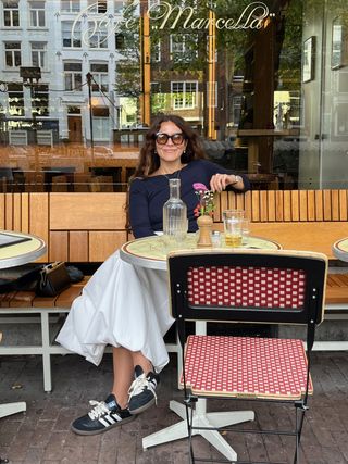 Alex DiCapo Patel sitting outside a restaurant wearing a chic fall outfit with Adidas Sambas.