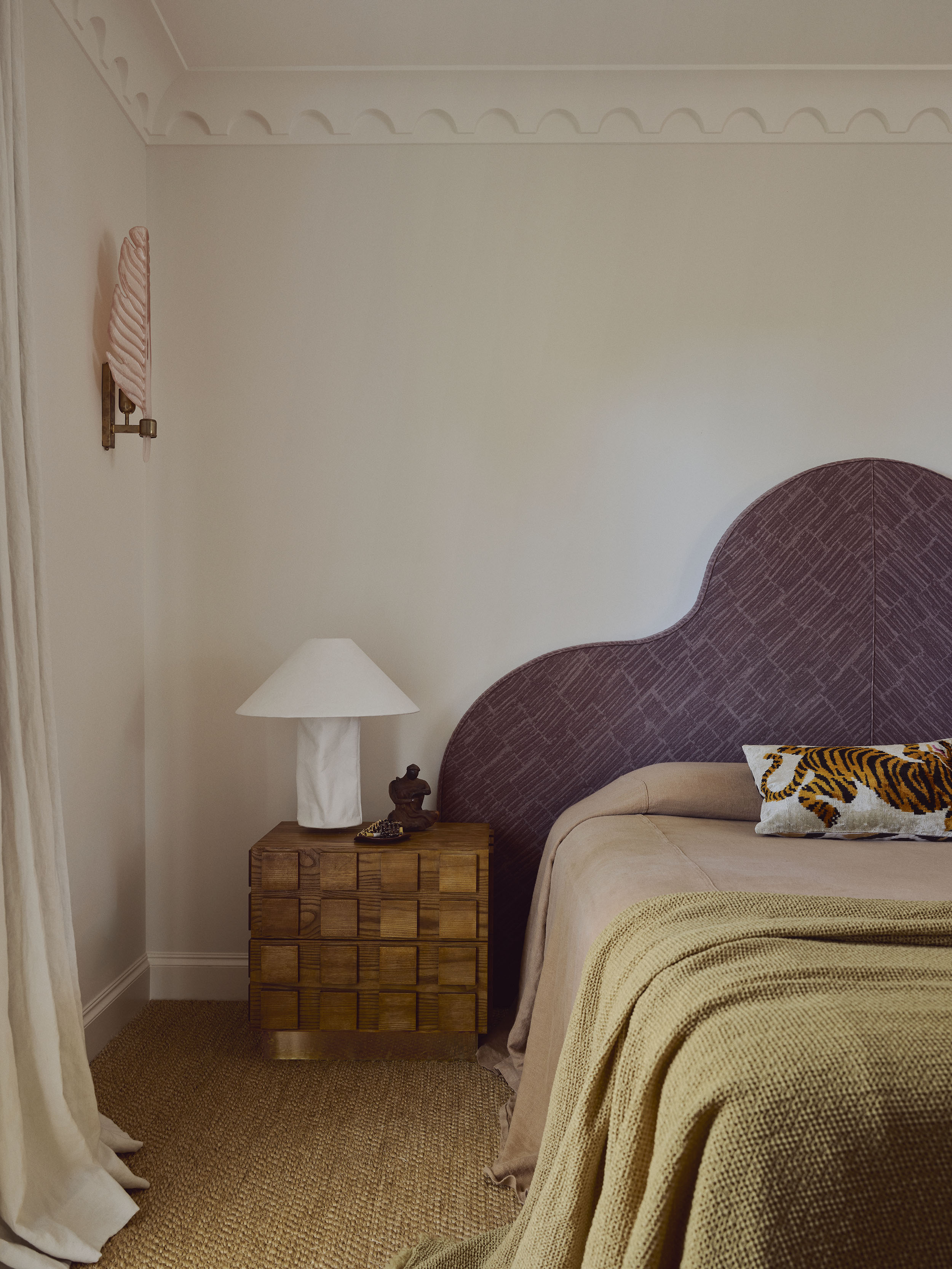 neutral bedroom with aubergine upholstered headboard, tan sheets and khaki throw