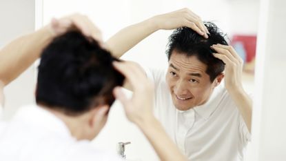 A man looking in the mirror, checking his hair line and contemplating using the best hair growth shampoo