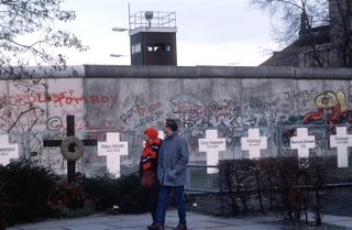 Following Germany's reunification, a couple reads grave markers of East Germans who died in an effort to escape over the Berlin Wall to the West.