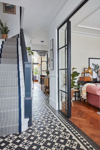 Hallway with original tile flooring, blue painted stairs with striped runner, and internal Crittal-style doors into living room