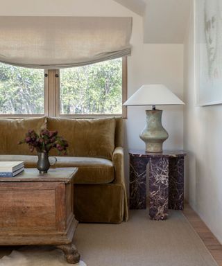 fall colors in a neutral living room with a deep ochre velvet couch, a burgundy marble side table and vintage wooden chest for a coffee table